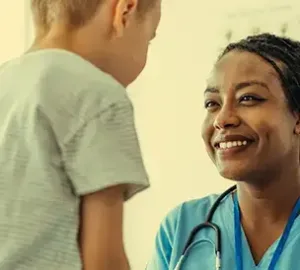 Female healthcare provider in blue scrubs smiling at a young boy during a check-up